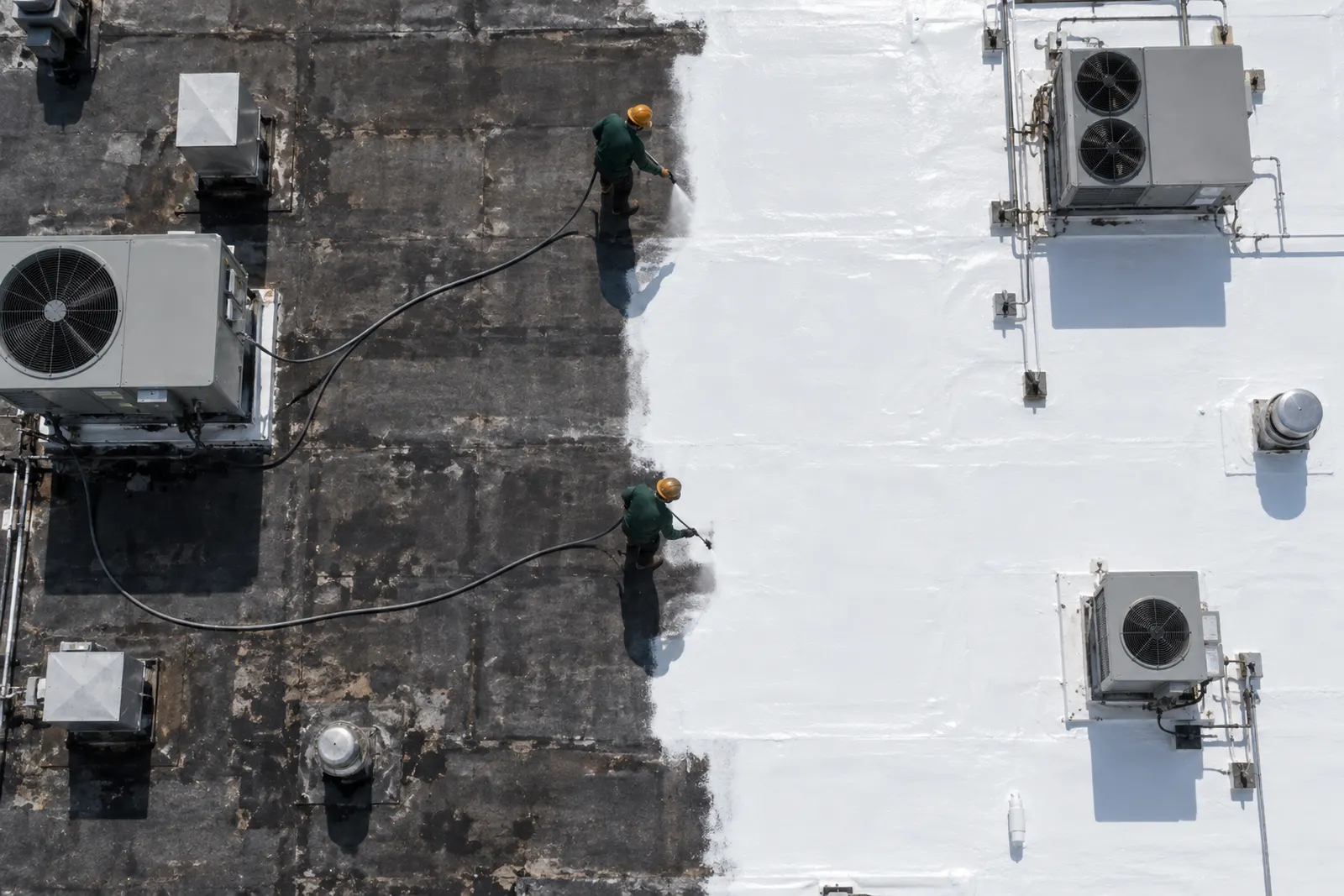 Aerial view of a low-slope roof half coated in white silicone around rooftop units