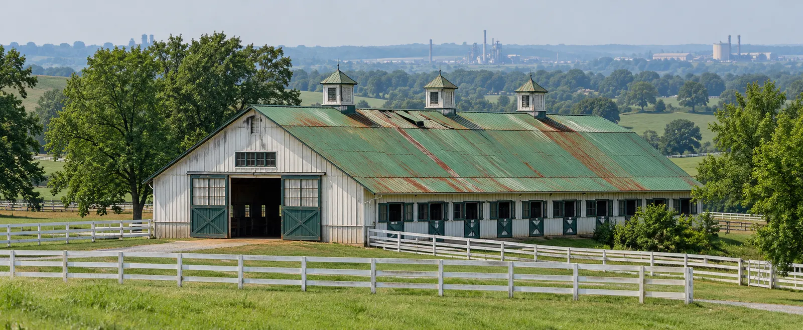 White horse barn with cupolas and a faded, rust-streaked green metal roof